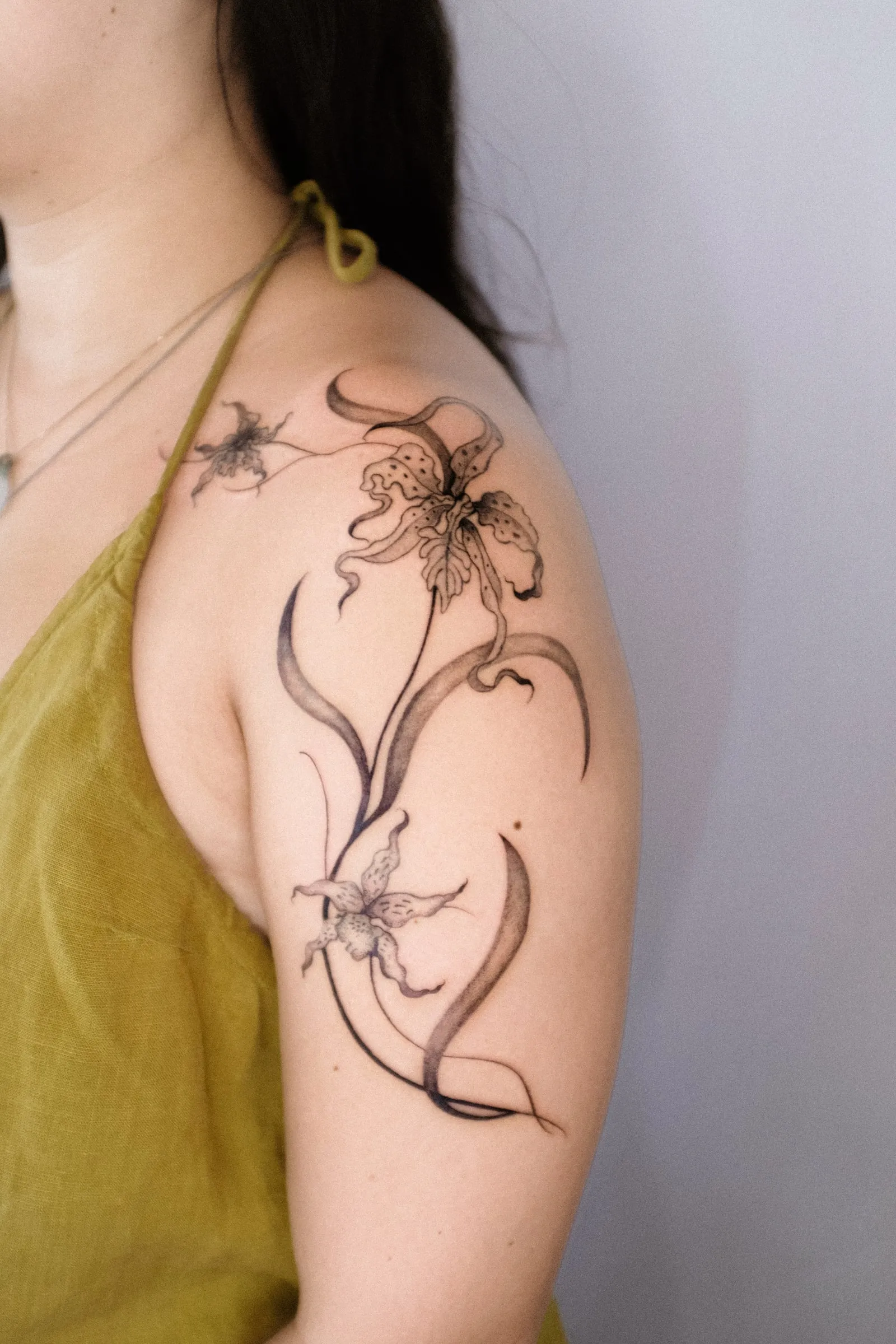 Finished shoulder tattoo of two orchids joined by long sweeping leaves and fine curved lines