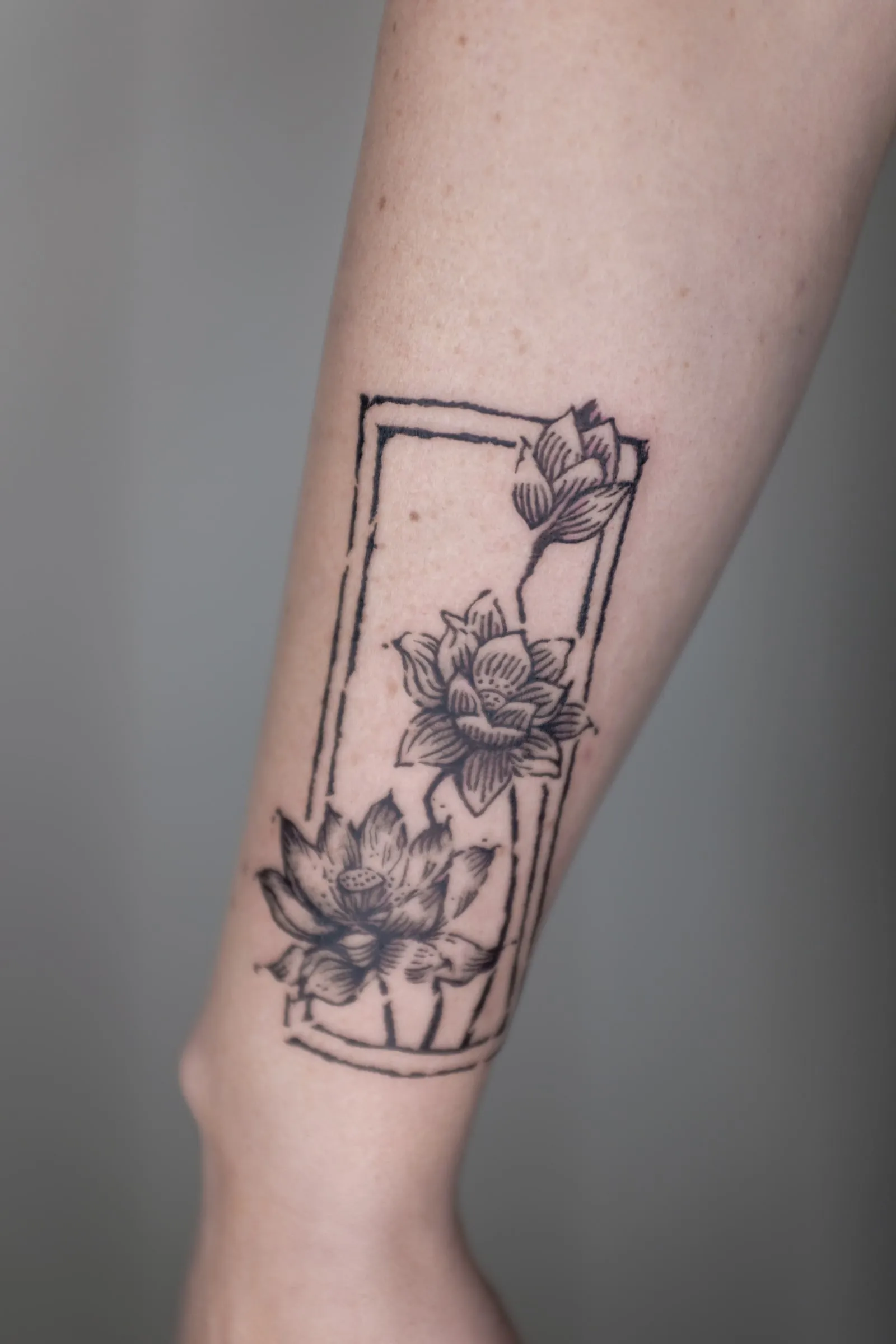 Finished forearm tattoo of three lotus flowers extending through a tall open black frame