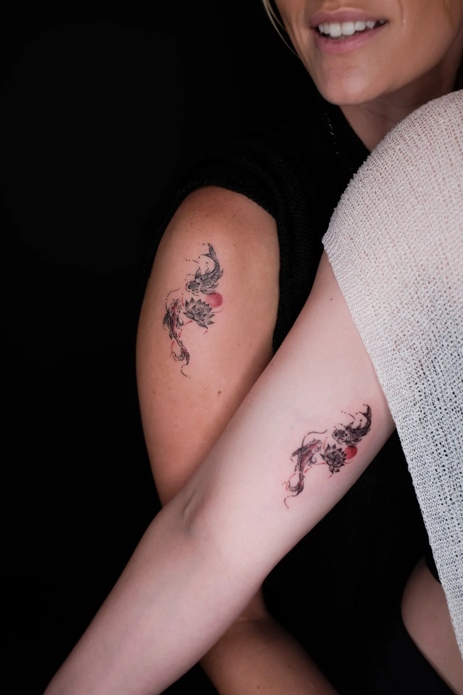 Two finished arm tattoos pairing swimming koi lotus flowers and small red sun accents