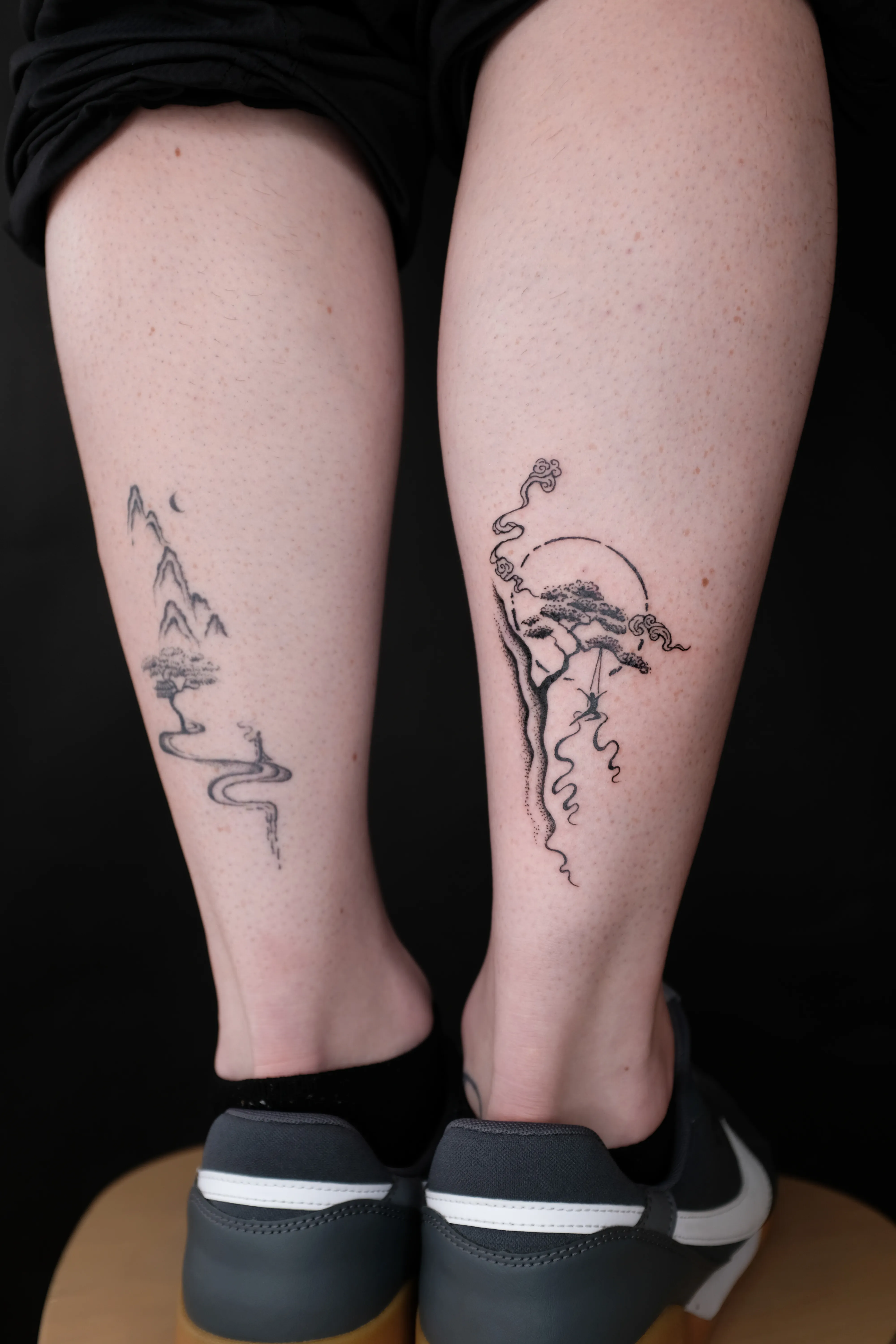 Finished calf tattoos with a winding mountain path and a pine tree beneath a circular sky