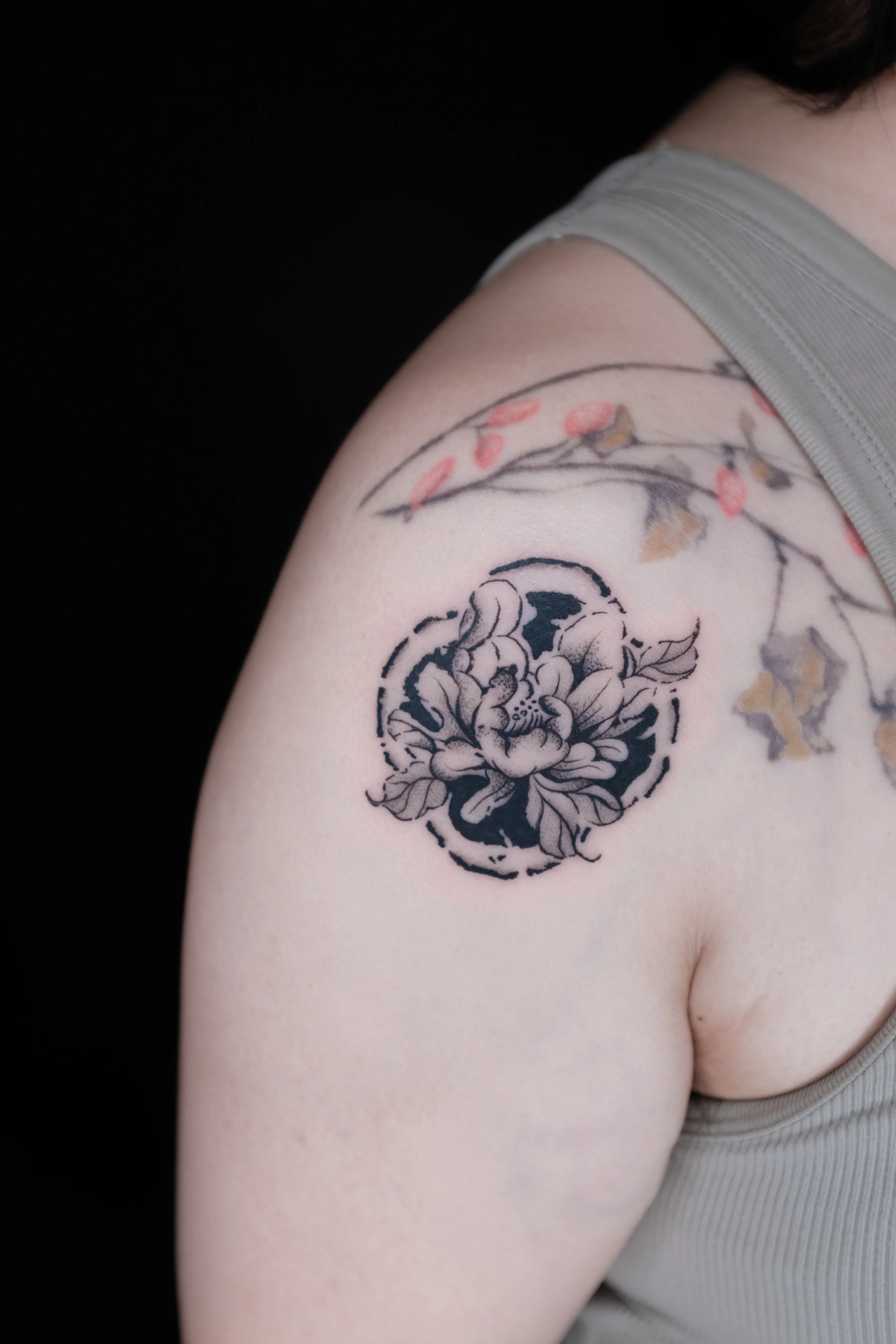 Finished shoulder tattoo of a peony and leaves set against a circular blackwork medallion