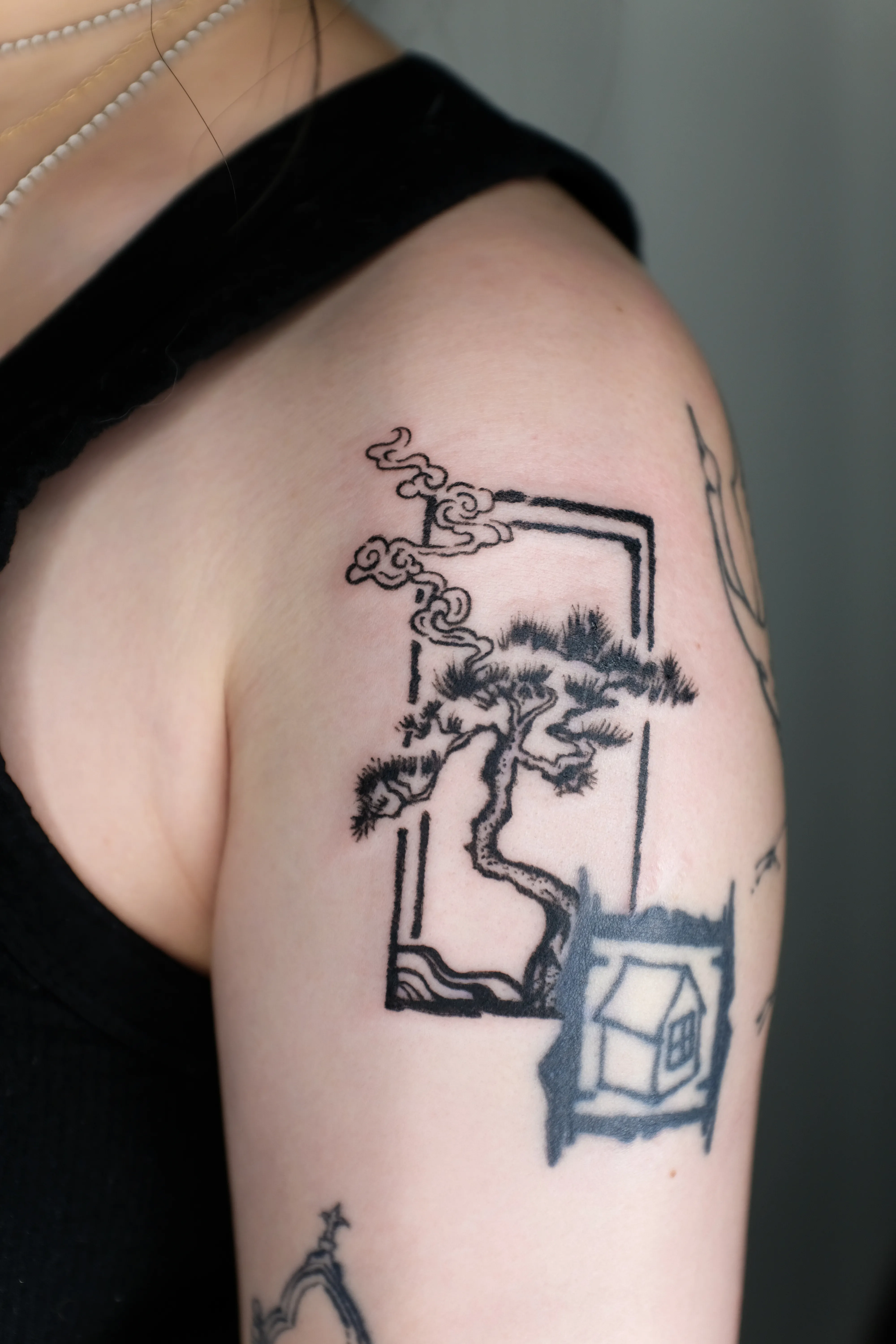 Finished shoulder tattoo of a windswept pine and curling clouds inside a broken rectangular frame