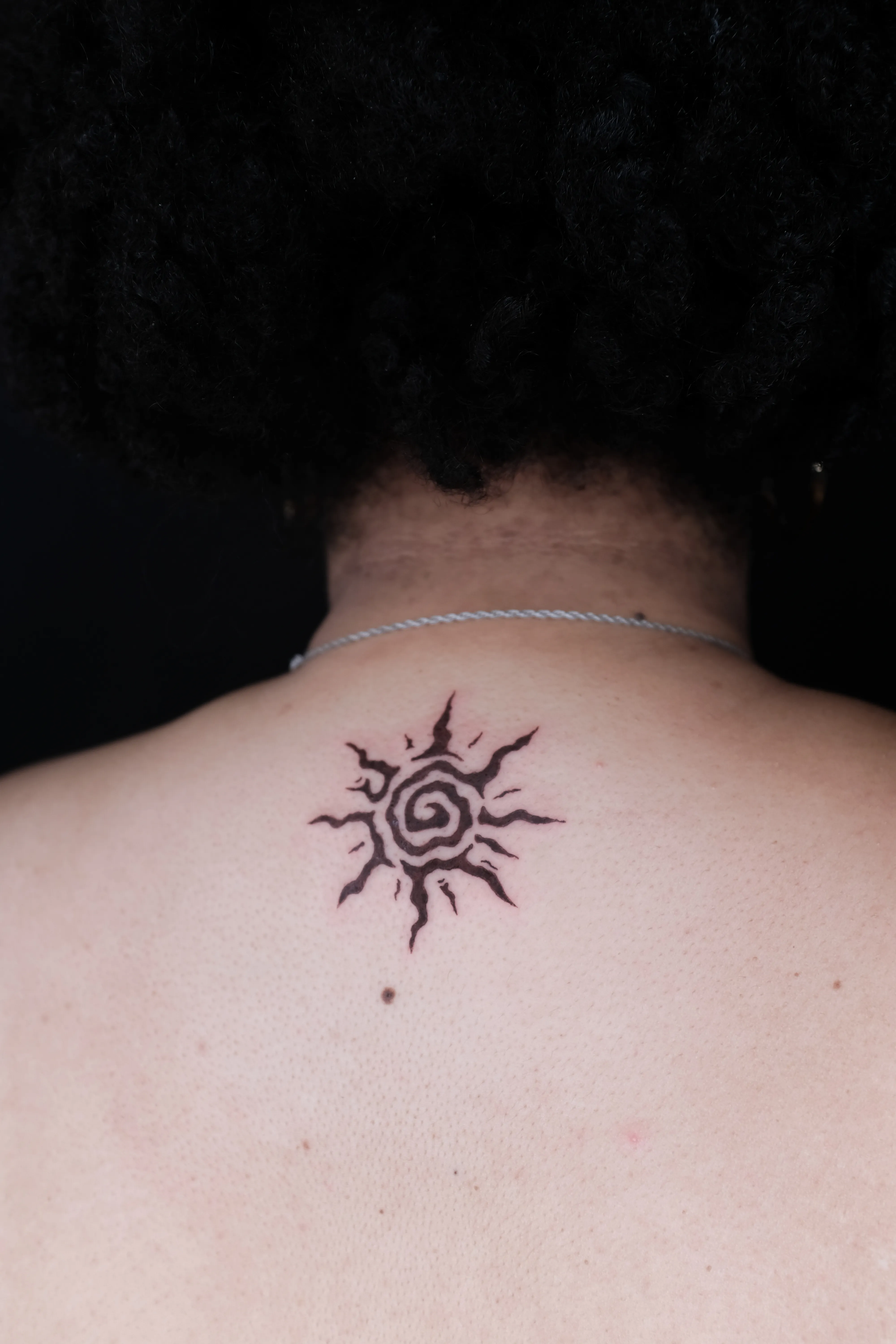 Finished upper-back tattoo of a bold black spiral sun with irregular flame-like rays