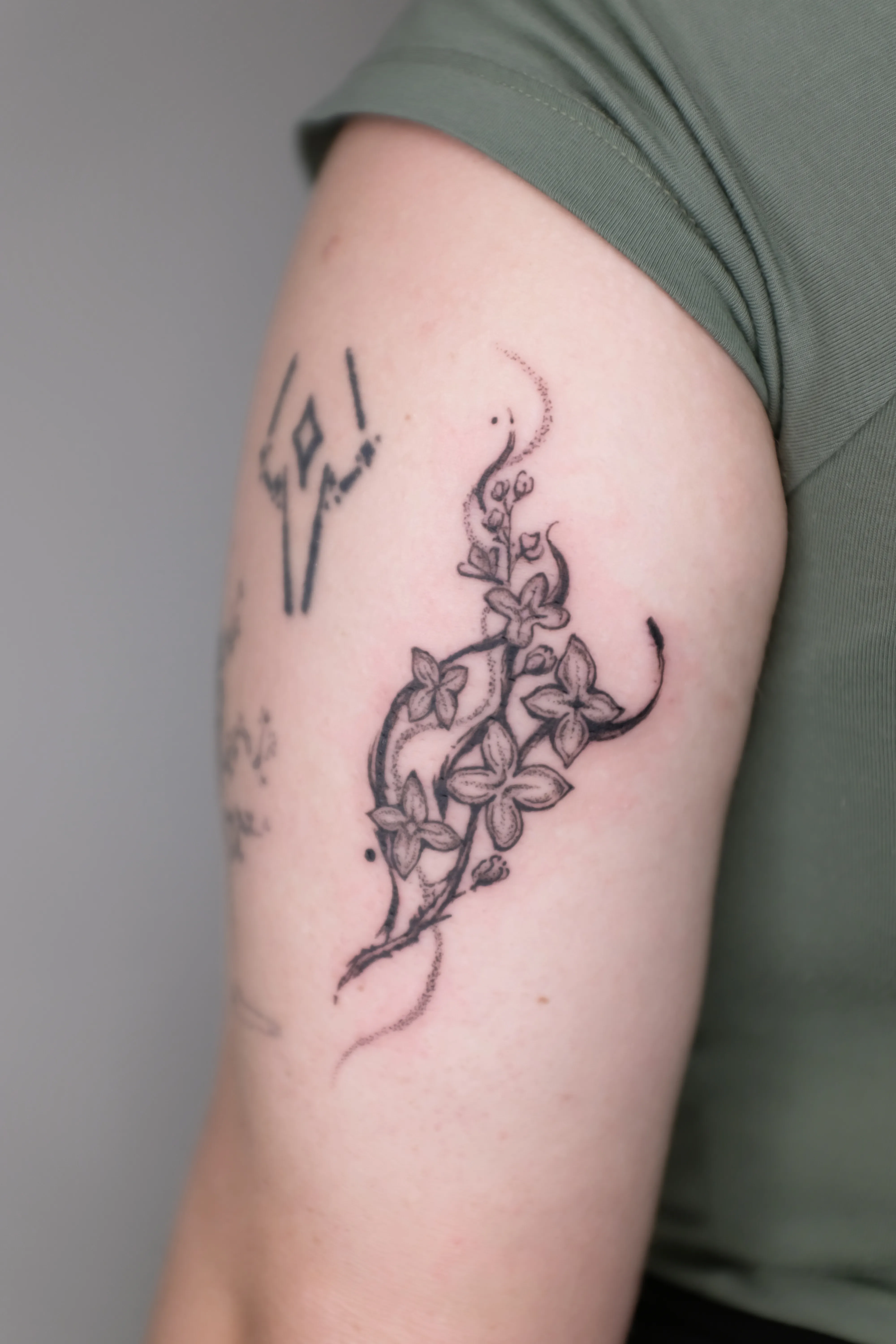 Finished upper-arm tattoo of small five-petal flowers growing along a curved stippled branch