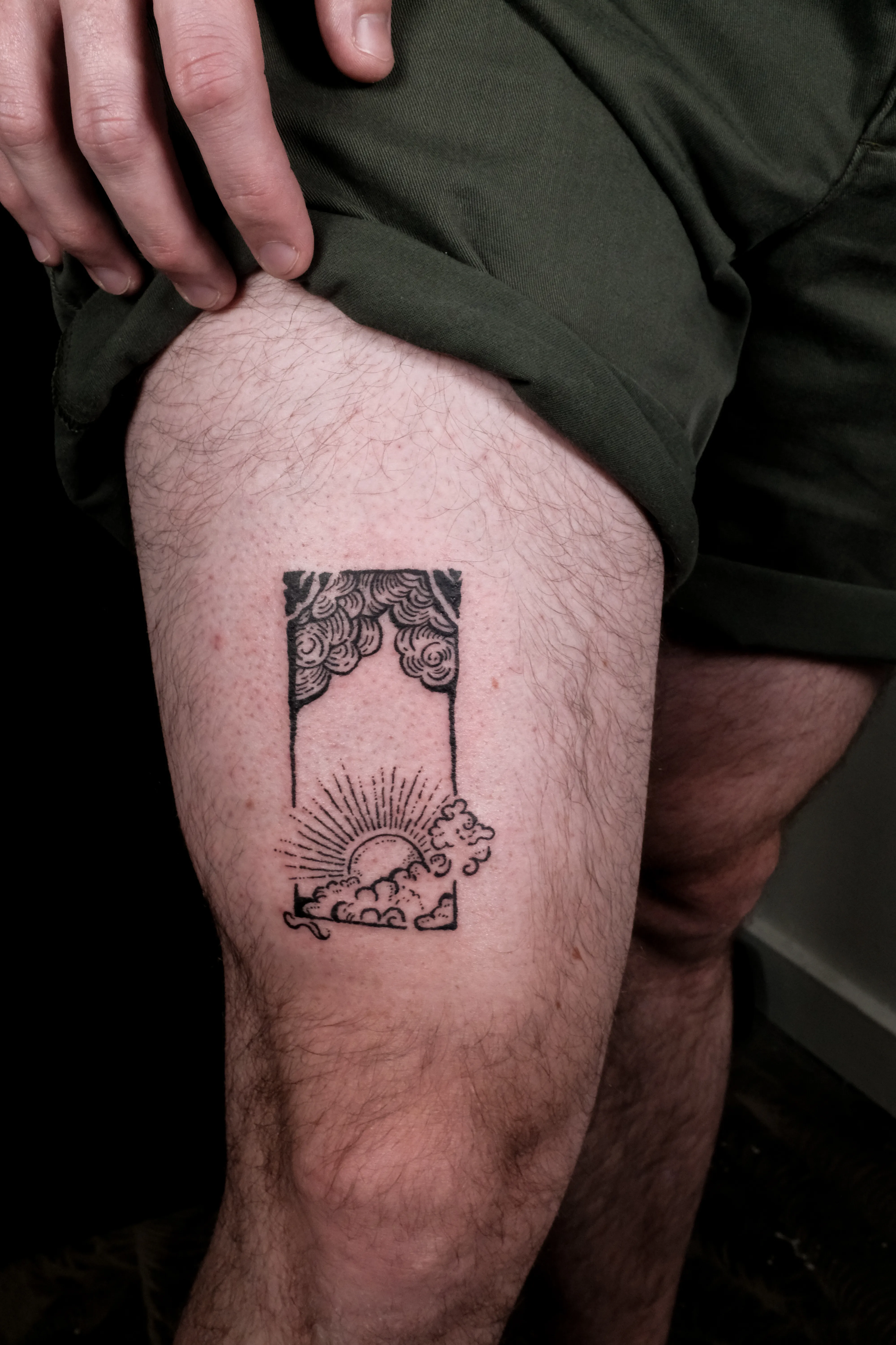Finished thigh tattoo of a rising sun and clouds breaking through a tall black frame